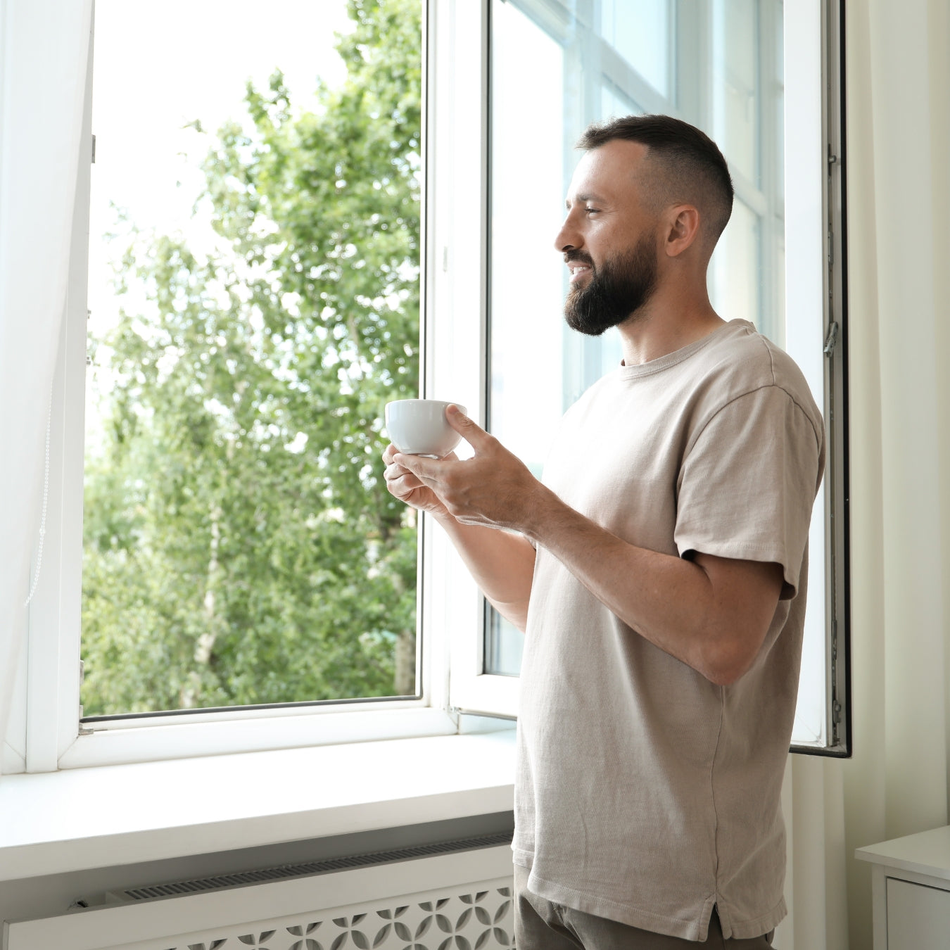 Bearded man enjoying coffee by bright window in modern home