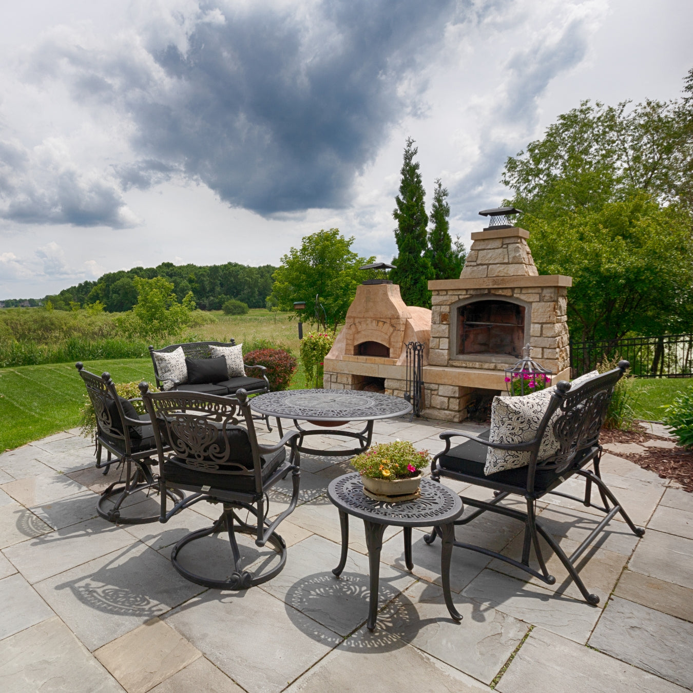 Outdoor patio with stone fireplace, tables, and chairs on a cloudy day.